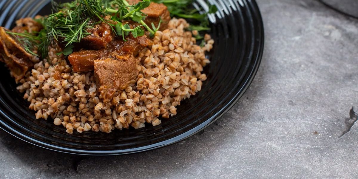 Delicious buckwheat with seasoned beef and greens served on a black plate.